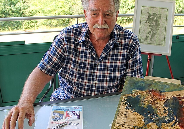 Wolfgang Moor auf seiner Terrasse mit seinen Arbeitsinstrumenten, dem Hohlmesser und dem Geissfuss, sowie einem Druckstock eines Hahnes. Im Hintergrund steht ein Holzschnitt eines Tango tanzenden Paares auf Tapete gedruckt. (Bild: mim) 